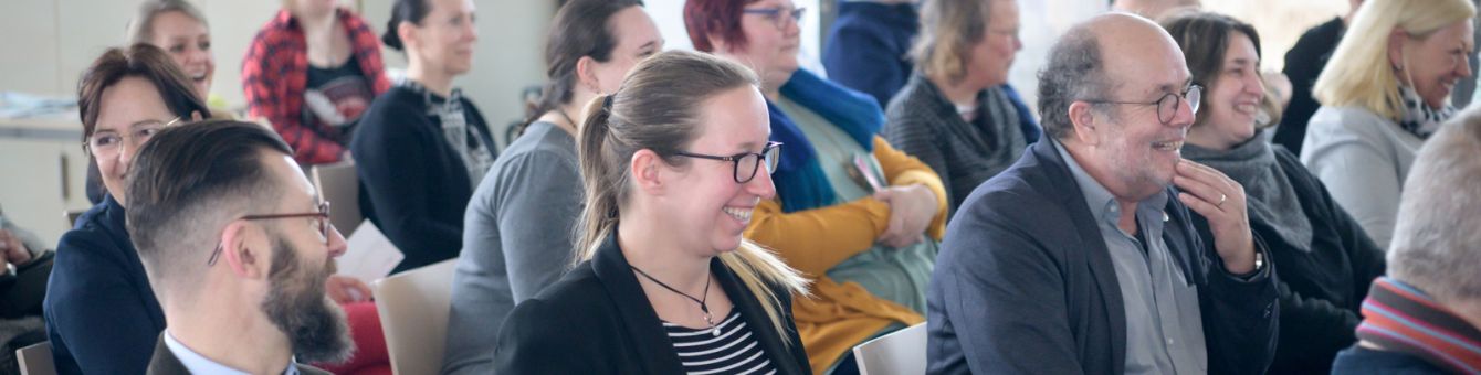 Menschen in Zuschauerreihen schauen lachend zur Bühne.