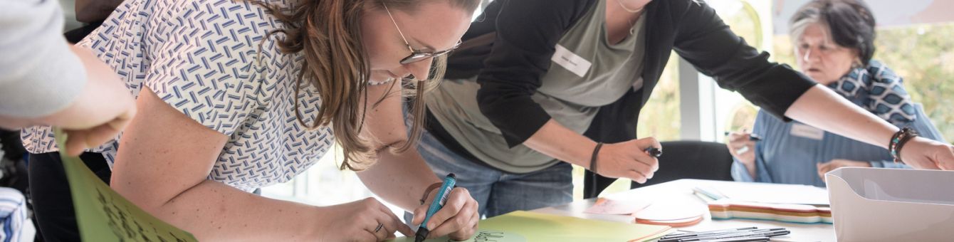 Drei Frauen beschriften bunte Moderationskarten an einem Tisch.